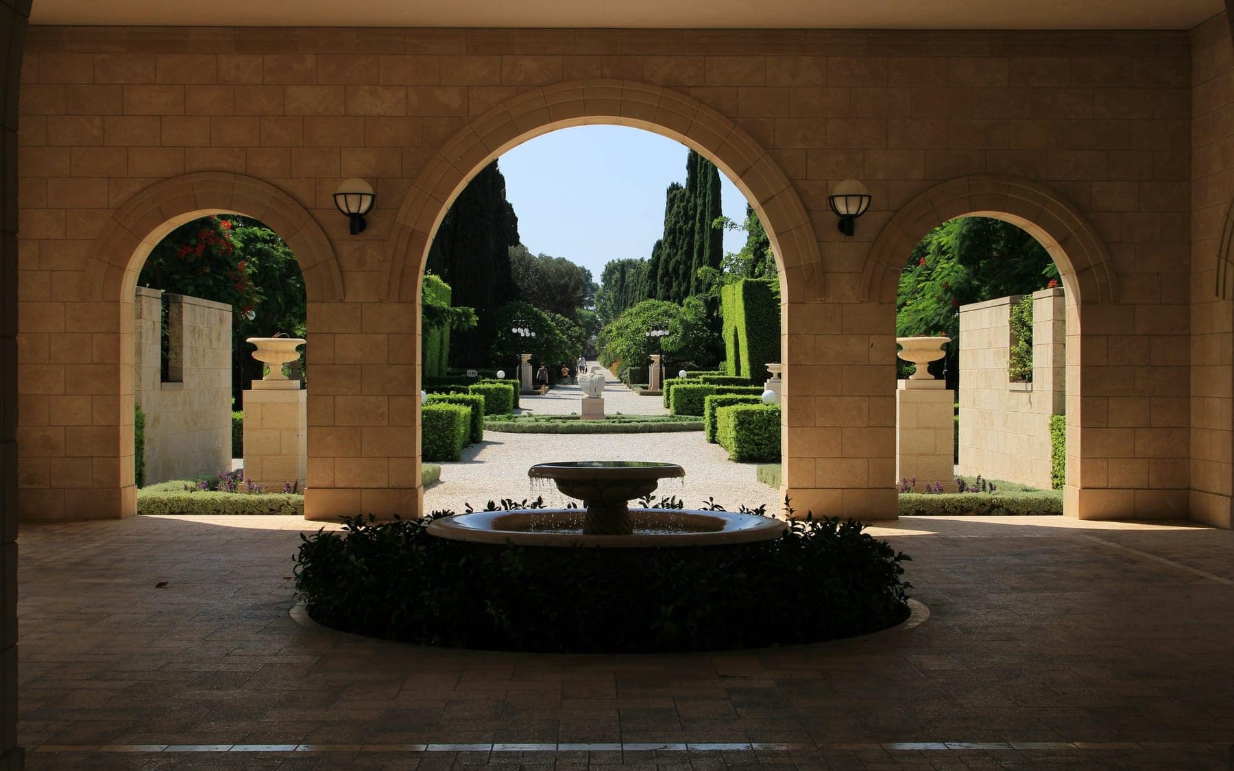 Portal de arcos de pedra emoldurando um jardim simétrico com fonte ao centro.